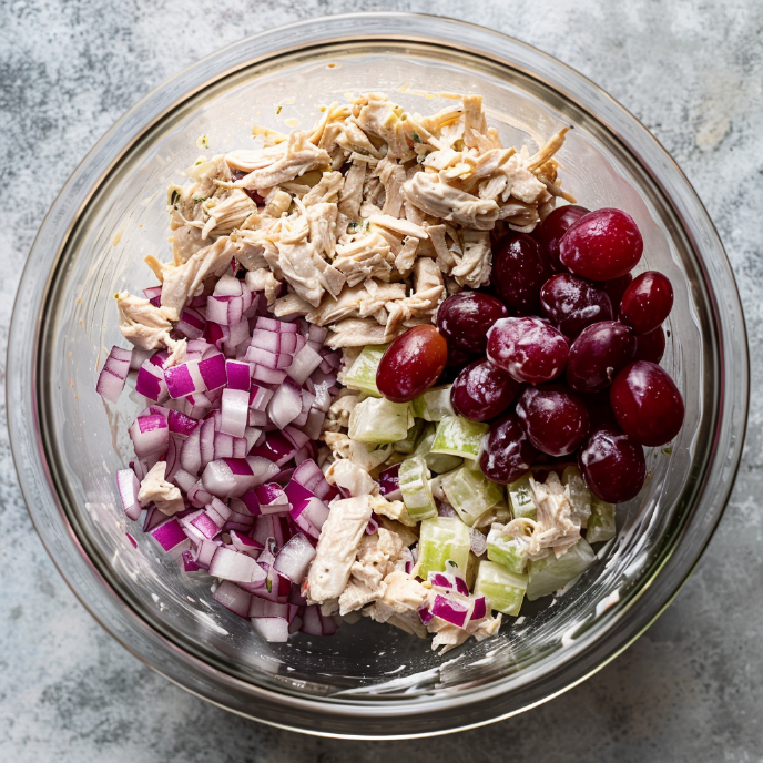 Chicken Salad ingredients with shredded chicken, diced red onion, grapes, and diced cucumber